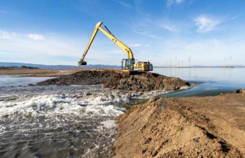 Bay waters pour into a 300-acre Ravenswood pond as an earthmover digs open the levee. Credit: Charles Anderson